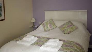 A neatly made bed with a white headboard, two decorative pillows, and two folded towels.