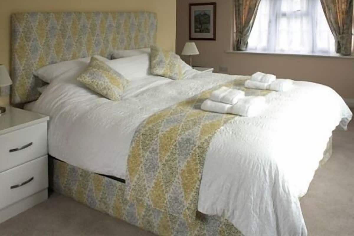 A neatly made bed with a patterned bedspread, pillows, and rolled towels.