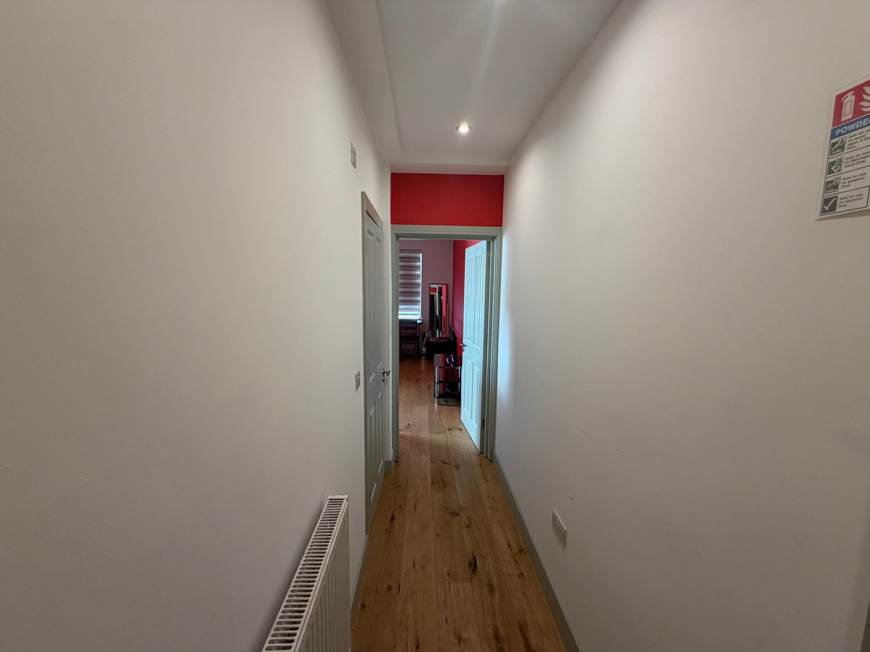 A narrow hallway with a radiator on the left and a door at the end.