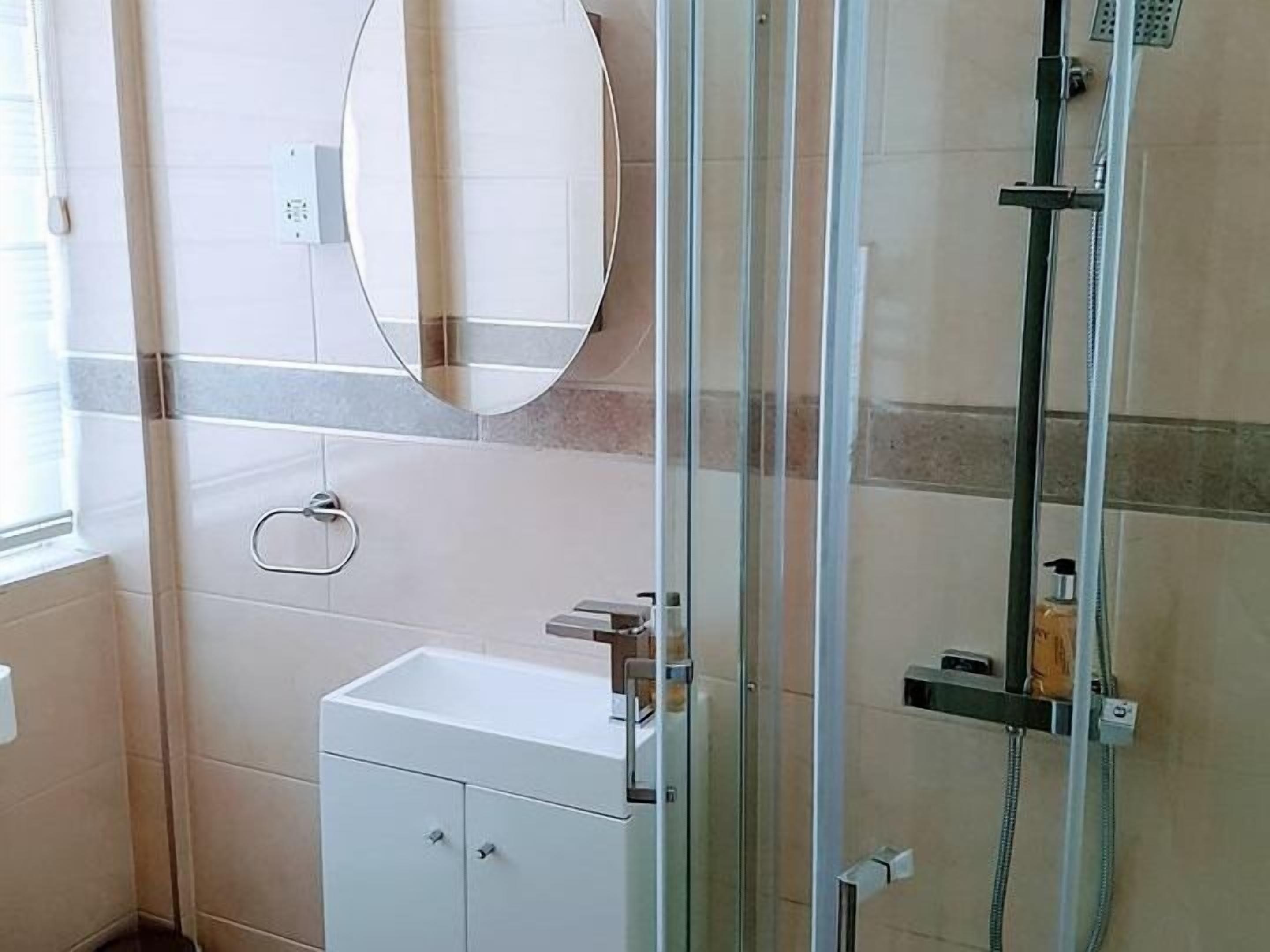 A bathroom with a glass shower enclosure, a white sink, and a mirror on the wall.