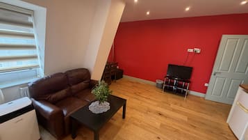 A living room with a brown leather sofa, a black coffee table with a decorative item, a television on a stand, and a red accent wall.