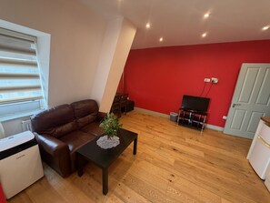 A living room with a brown leather sofa, a black coffee table with a decorative item, a television on a stand, and a red accent wall. - Forest House Hotel (London)