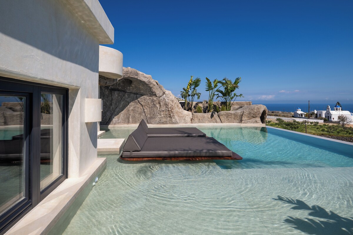 A modern pool with clear water, a lounge area, and a view of the ocean and distant buildings.
