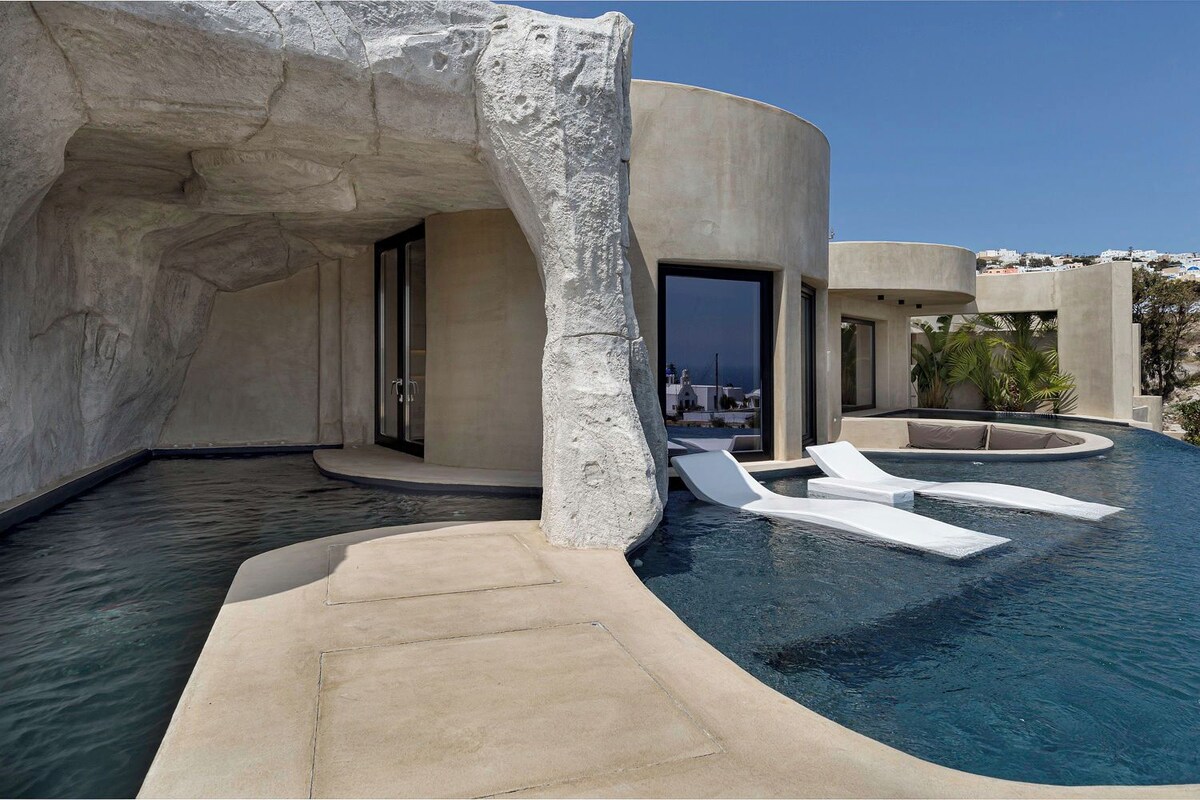 A modern pool area with a unique rock formation, clear blue water, and lounge chairs.