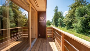 A wooden deck with glass railings overlooking a forested area.