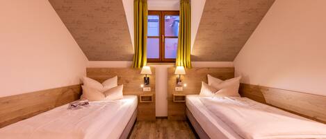 A room with two beds, wooden headboards, a window with yellow curtains, and bedside lamps.