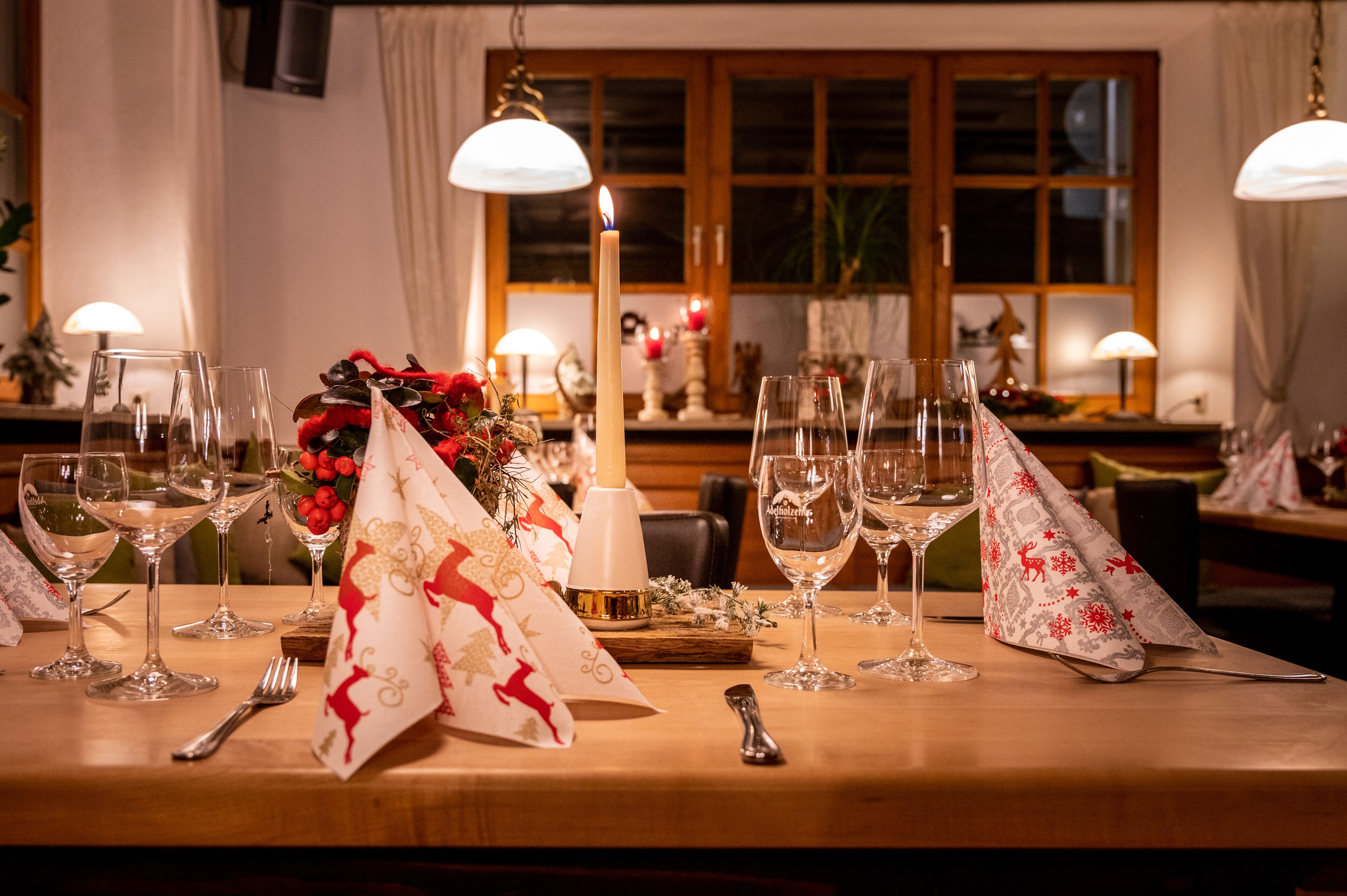 Una tavola imbandita con bicchieri da vino, una candela accesa e decorazioni festive.