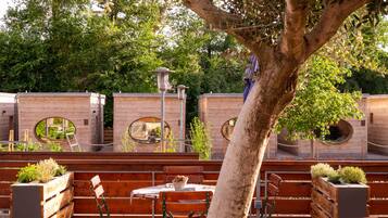 Un espace extérieur aménagé avec des bancs en bois et des jardinières, entouré de murs en briques percés de fenêtres rondes.