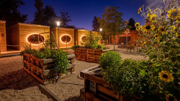 A courtyard with wooden planters, a seating area, and a building with circular light fixtures.
