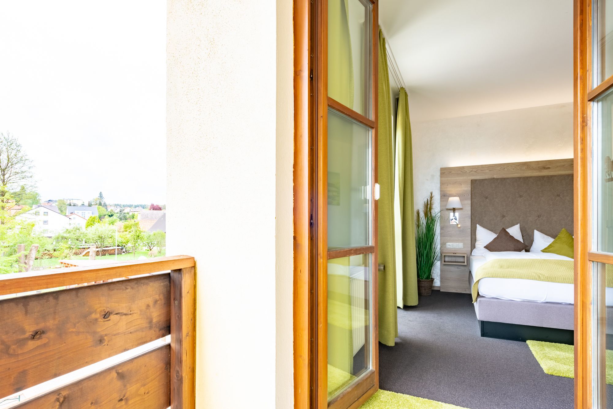 A hotel room with a bed, a nightstand, a lamp, and a view of the outside.