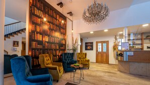 A spacious lobby with a large bookshelf, comfortable seating, a chandelier, and a reception desk.