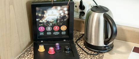 Una cafetera con pantalla, una tetera y un juego de cápsulas de café sobre una mesa.