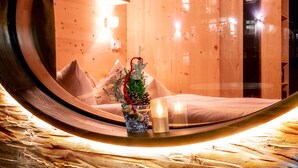 A cozy room with a wooden interior, a bed with a white mattress, a small potted plant, and a candle on a wooden surface.
