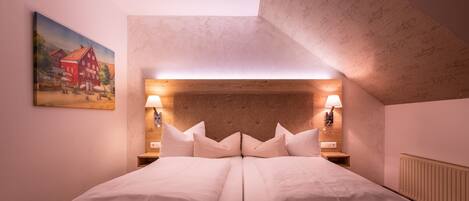 A double bed with a wooden headboard, two bedside lamps, and a painting on the wall.