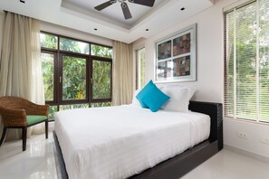 A bedroom with a bed, a chair, a ceiling fan, and large windows.