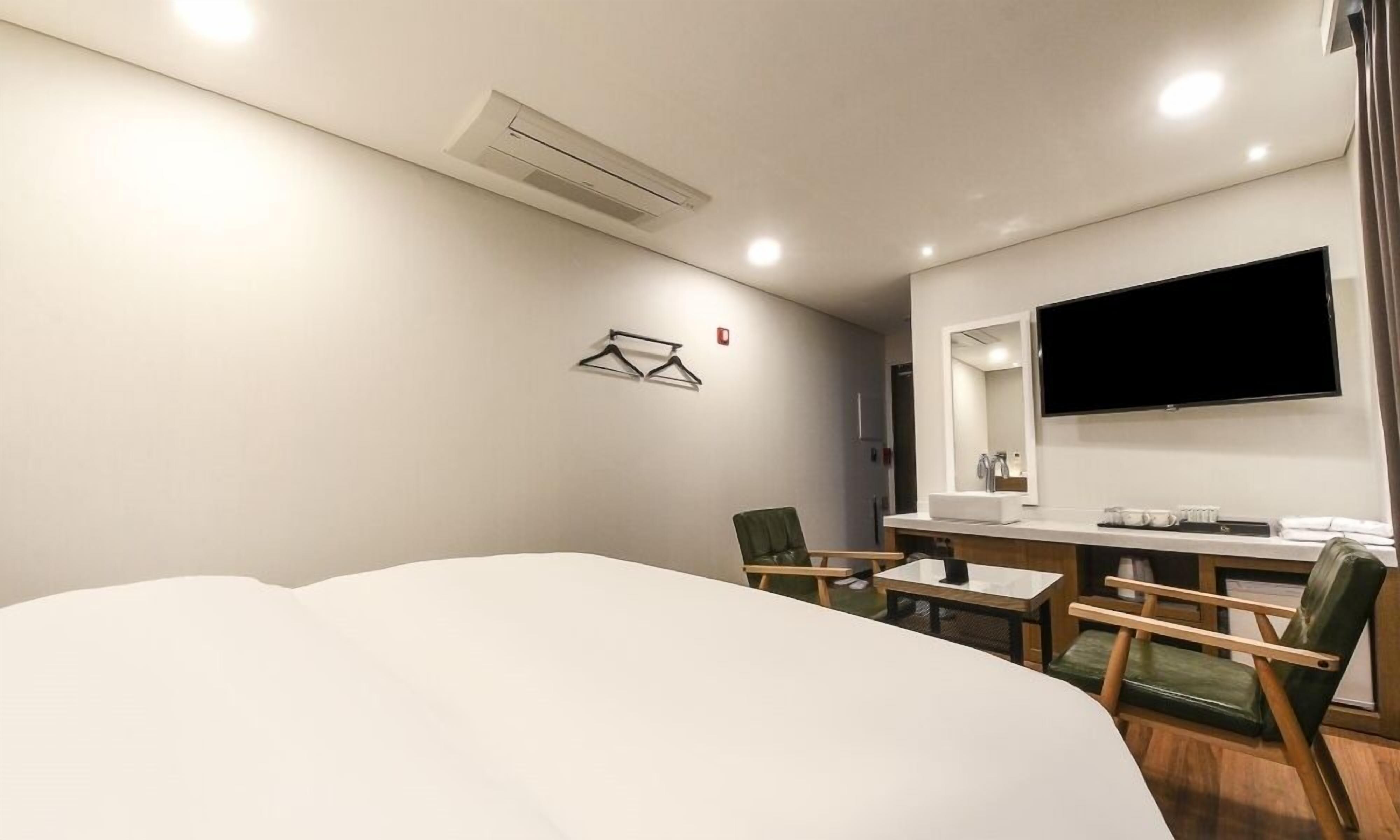 Habitación de hotel con cama, escritorio con lavamanos, dos sillas, televisor montado en la pared y aire acondicionado.