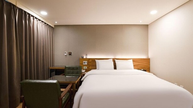 A hotel room with a large bed, a desk with a chair, and a window with curtains. - Anyang CNC Hotel (Anyang)
