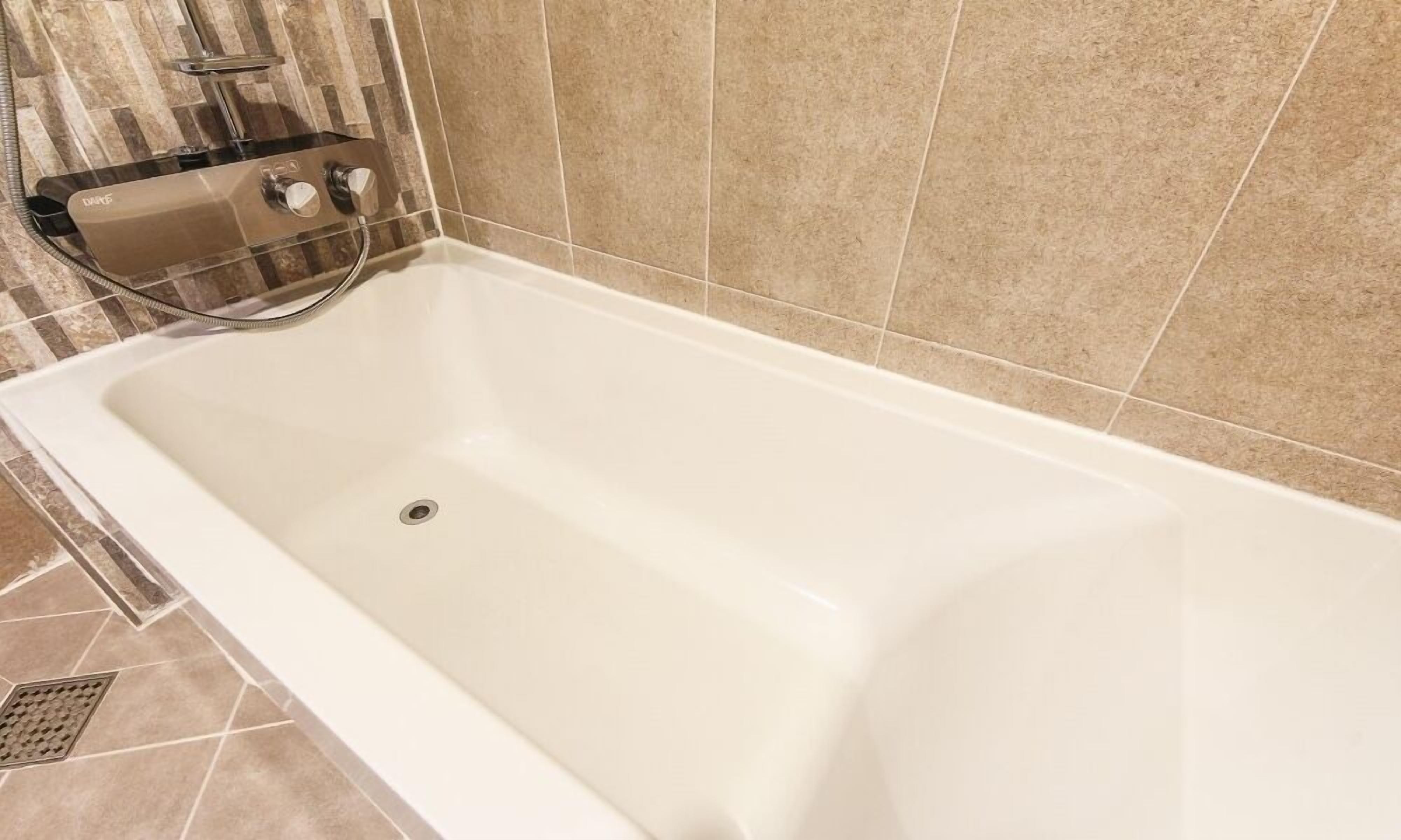 Una bañera blanca con cabezal de ducha integrado y mandos.