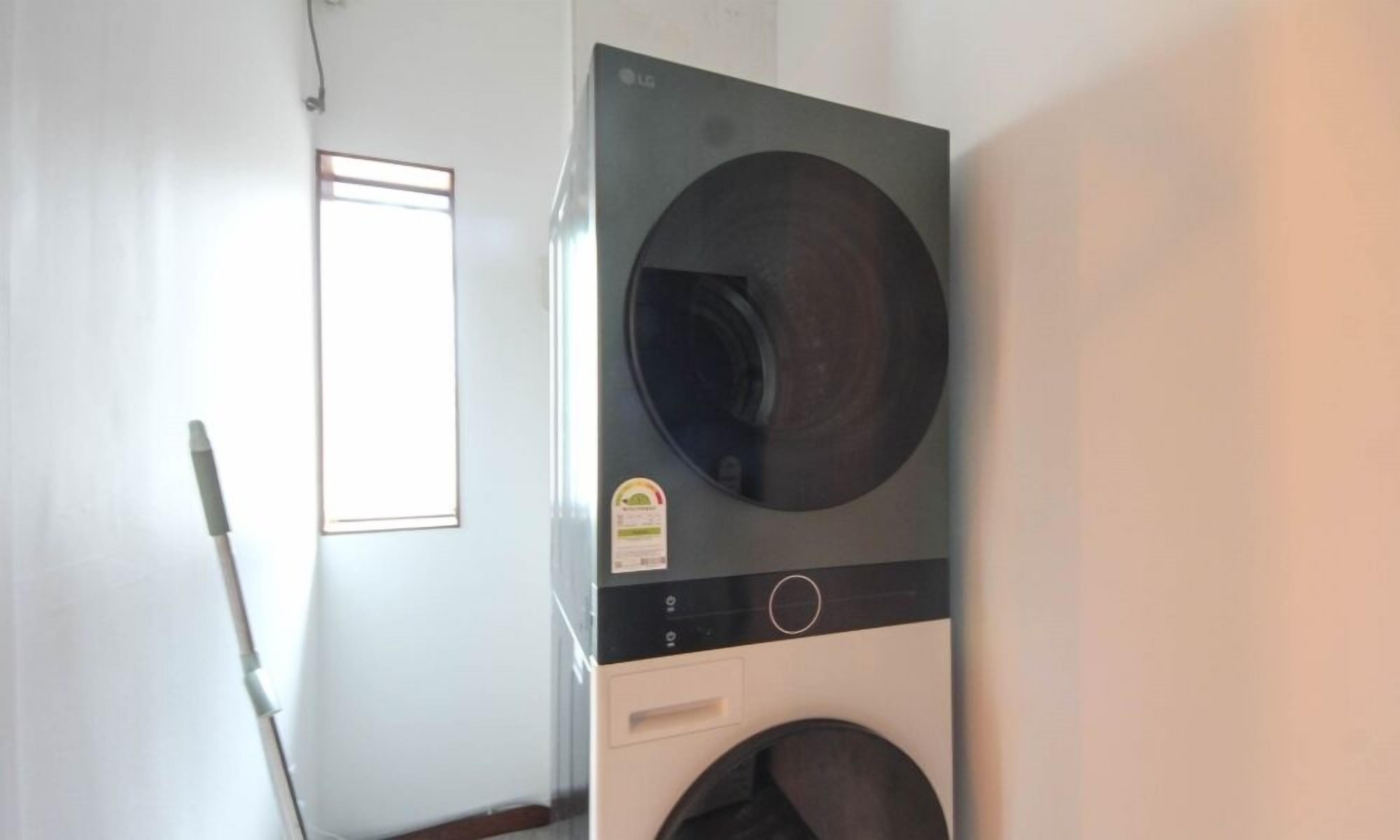 Une buanderie équipée d’un lave-linge et d’un sèche-linge à chargement frontal, d’une fenêtre et d’un balai appuyé contre le mur.