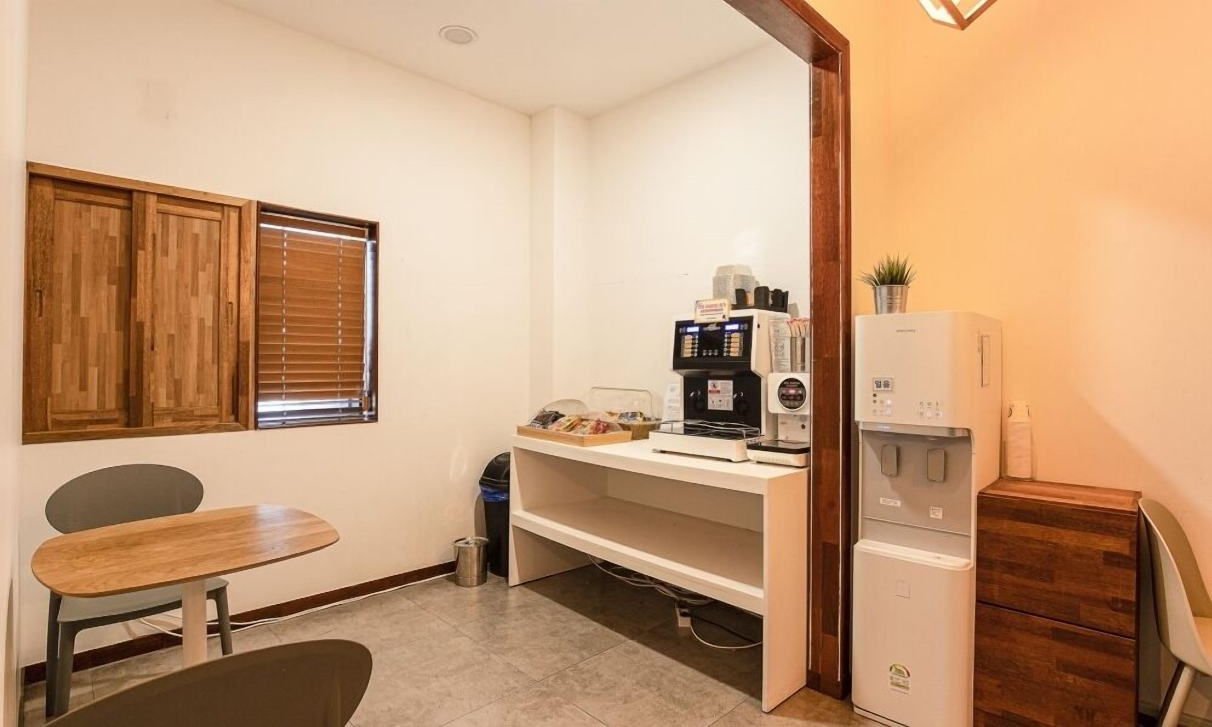 Una kitchenette compacta con cafetera, un refrigerador pequeño y un comedor con mesa y sillas.