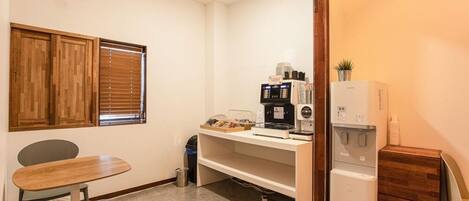 Una kitchenette compacta con cafetera, un refrigerador pequeño y un comedor con mesa y sillas.