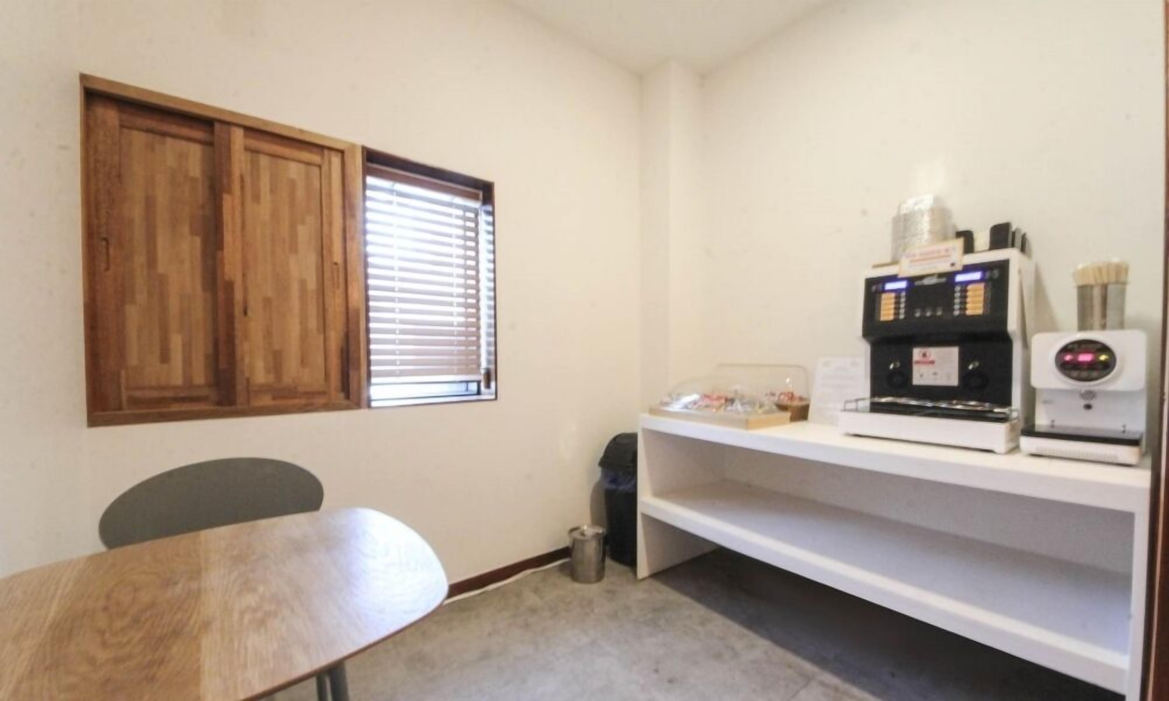 Una habitación pequeña con un armario de madera, una ventana con persianas, una cafetera y un cubo de basura.
