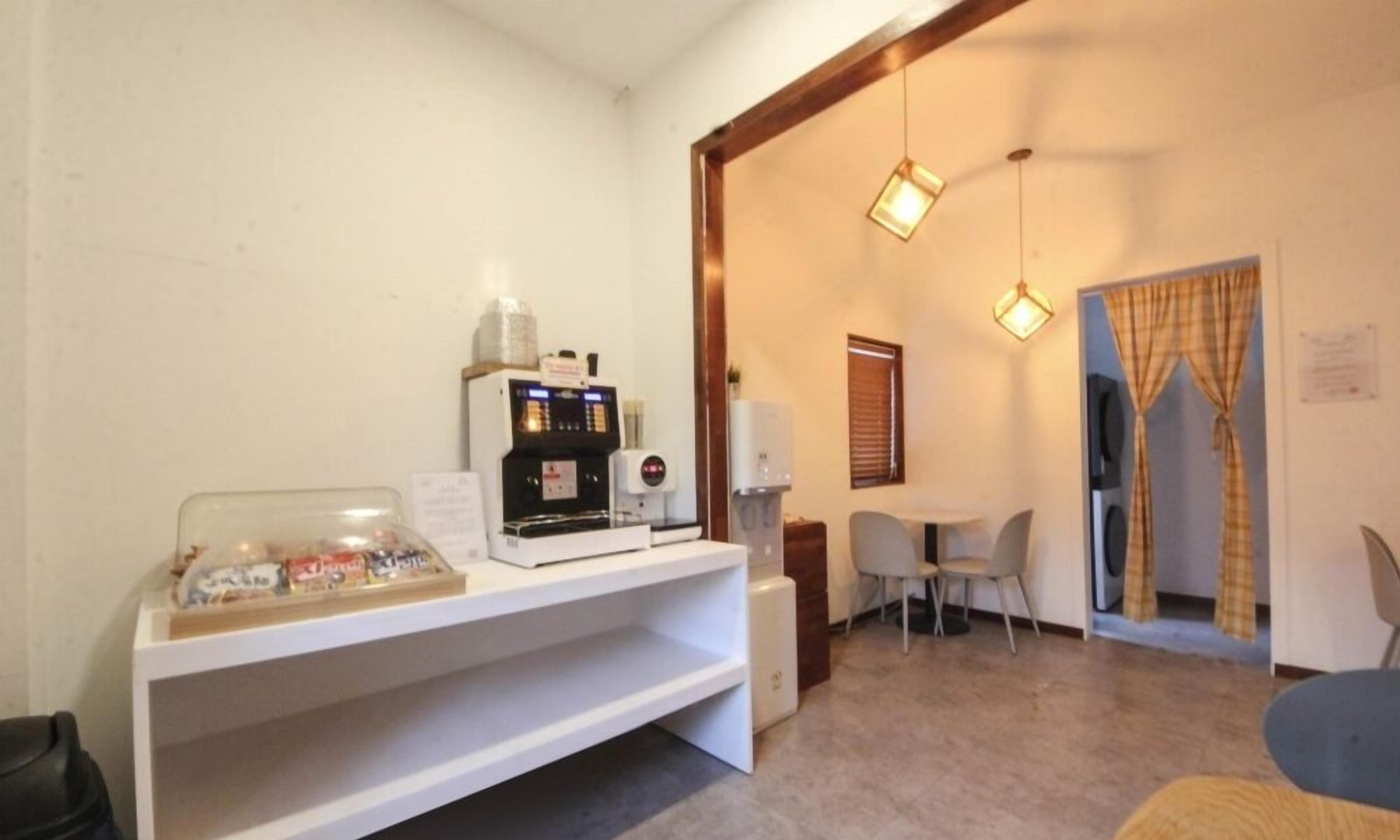 A small kitchenette with a coffee machine, a microwave, and a glass jar of snacks. There is a small table and chairs in the background.