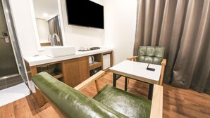 A compact room with a flat-screen TV mounted on the wall, a sink, a mirror, a small table with a chair, and a green cushioned bench. - Anyang CNC Hotel (Anyang)