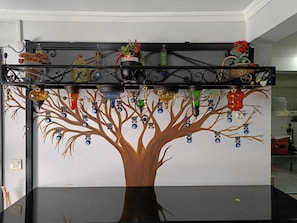A room with a black table, a wall-mounted shelf with various items, and a tree mural.