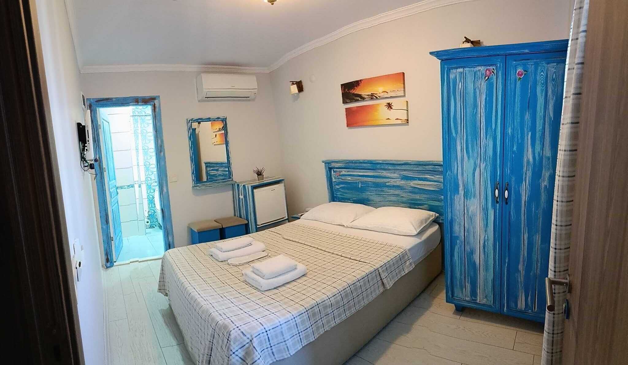A bedroom with a bed, a wardrobe, a small bedside table, and a wall-mounted mirror.