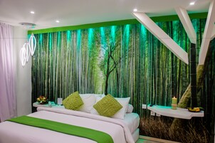 A modern bedroom with a green-themed wall, a bed with white bedding and green pillows, a bedside table with a phone and a candle, and a bamboo forest mural.