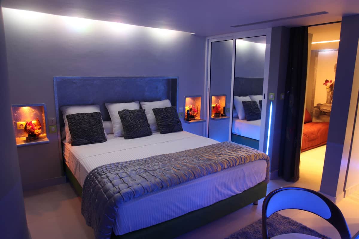 Une chambre moderne avec un grand lit, des tables de chevet avec des lampes et une porte coulissante donnant sur une autre pièce.