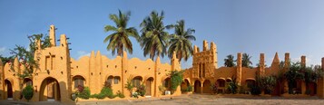 A traditional building with multiple arches and a central tower, surrounded by palm trees.