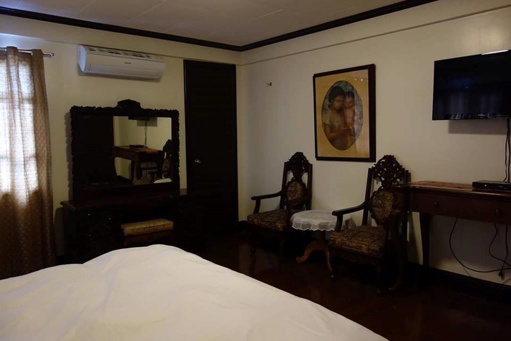 A hotel room with a bed, a desk, a chair, an air conditioner, a television, and a painting on the wall.