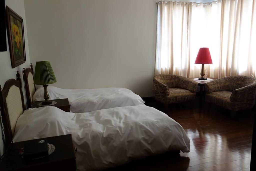 A hotel room with two beds, a green lamp, a red lamp, and a chair by the window.