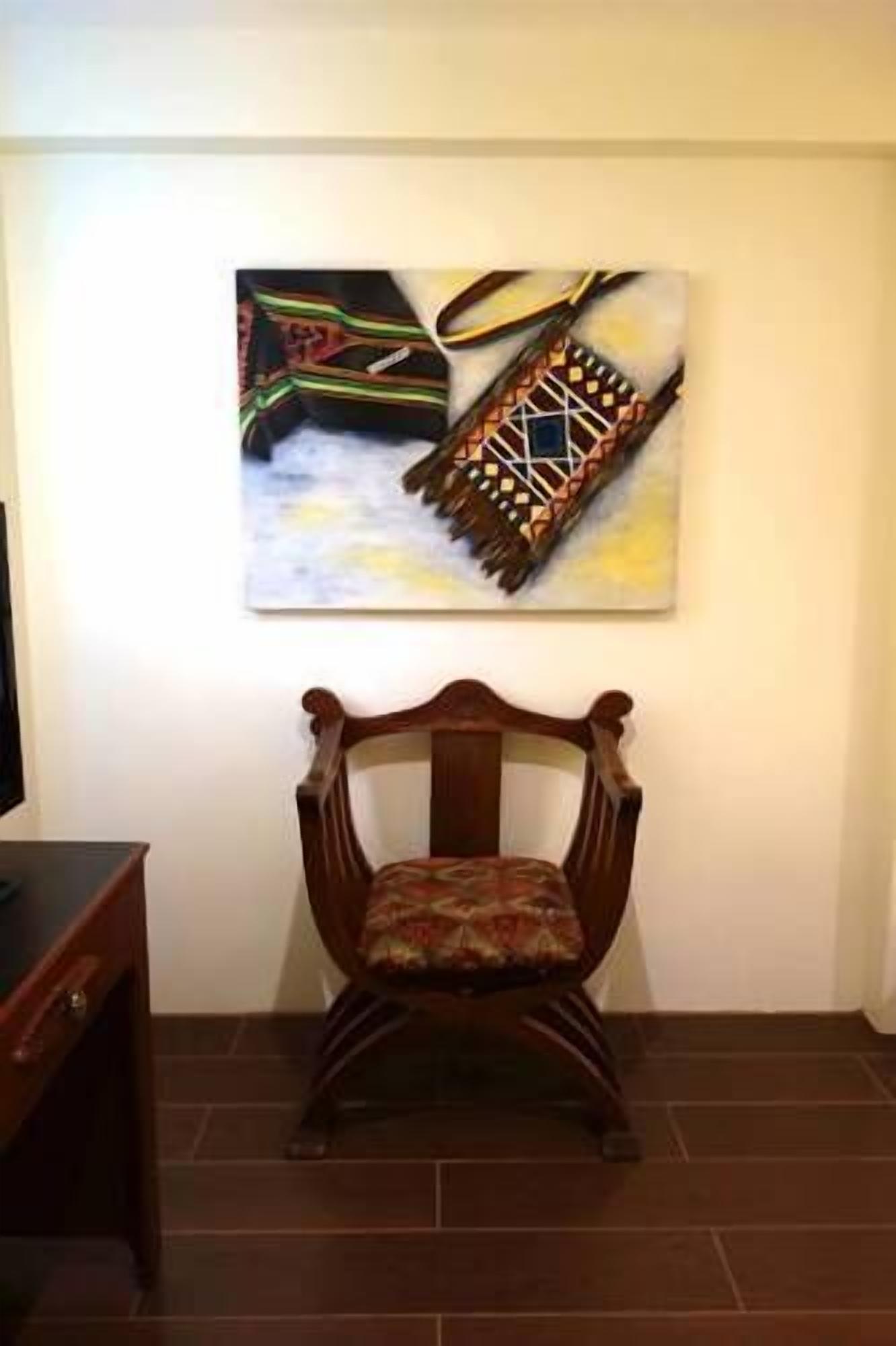 A wooden chair with a patterned cushion in a room with a tiled floor and a wall-mounted painting.