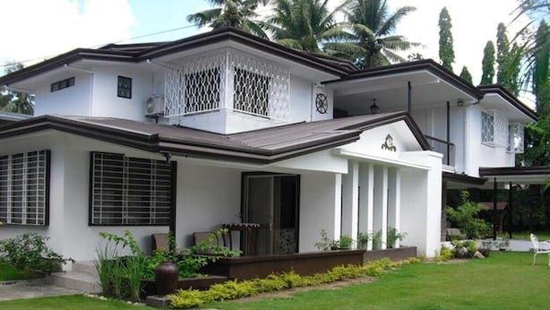 A two-story house with a white exterior, a balcony with a lattice design, and a well-maintained lawn with stepping stones.