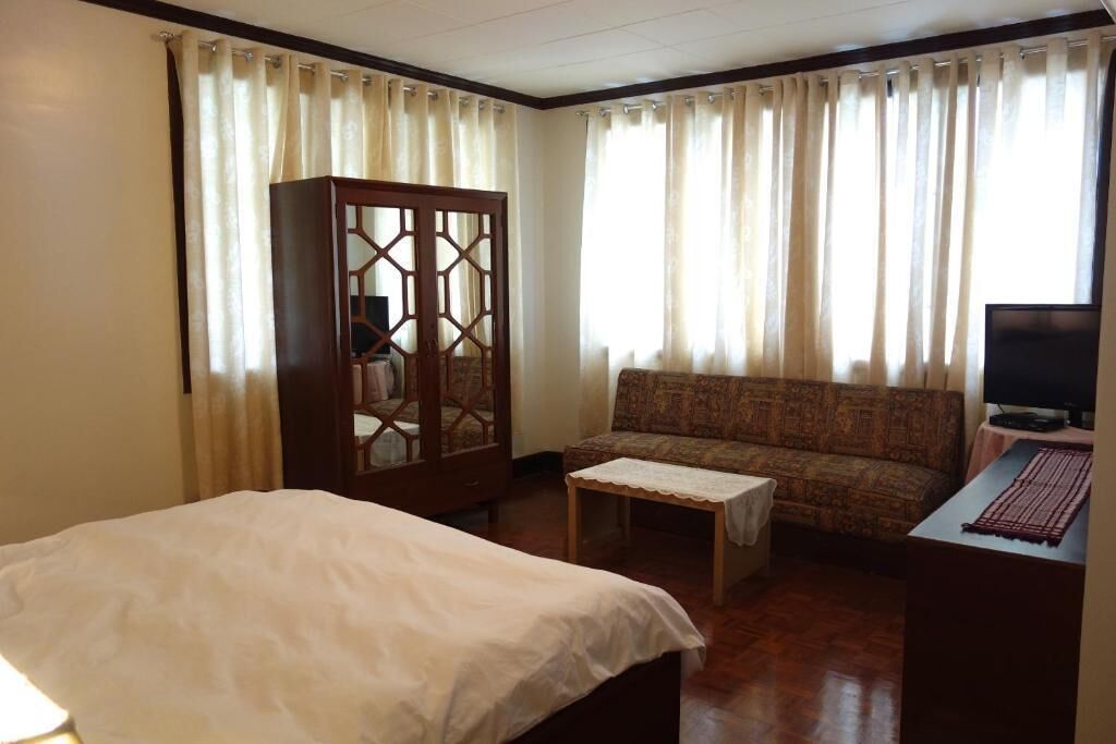 A hotel room with a bed, a sofa, a TV, and a cabinet.