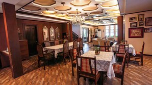A dining area with wooden flooring, tables with white tablecloths, and chairs with patterned cushions.