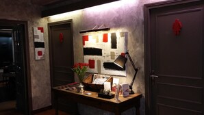 A reception desk with a lamp, a vase of red flowers, and a small plant. There are two doors with red symbols on them. - Hôtel Restaurant Le relais de la Sans Fond (Fenay)
