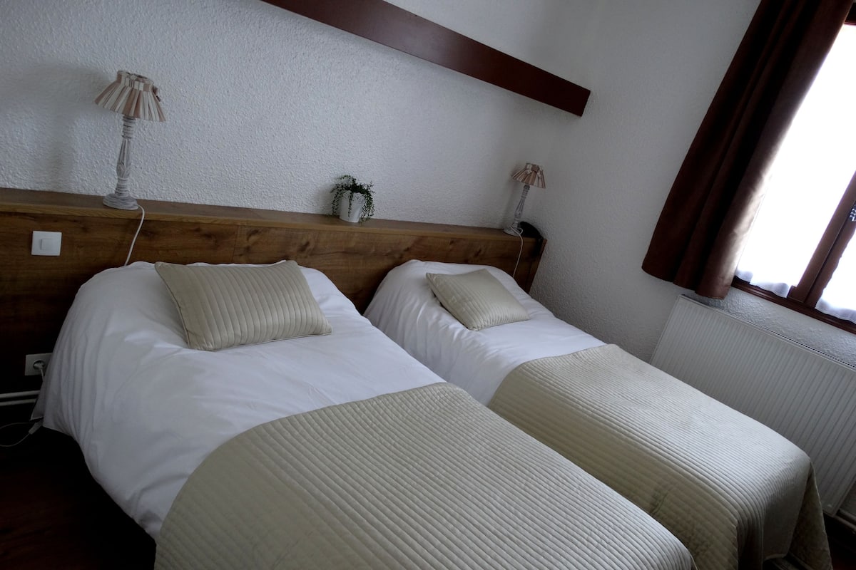 Un lit double avec une tête de lit en bois, deux tables de chevet et une petite plante en pot.