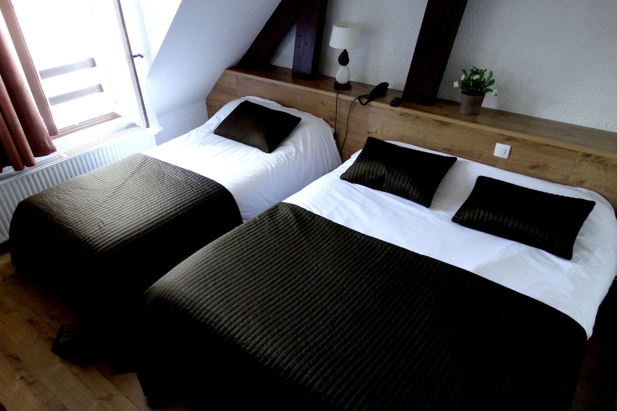 Deux lits simples avec une literie noire et blanche, une tête de lit en bois, une lampe de chevet, un téléphone et une petite plante sur une table de chevet en bois.