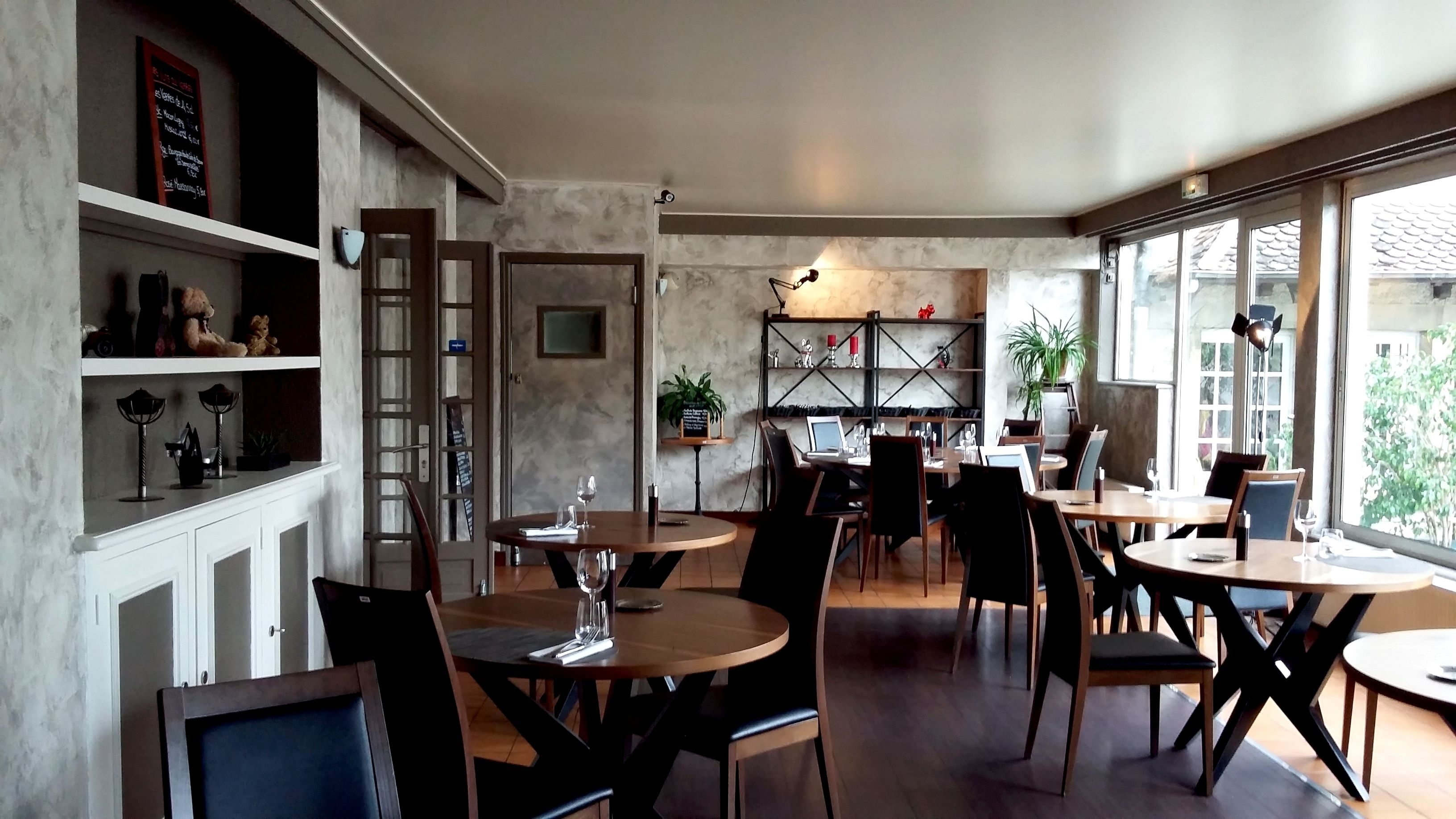 A restaurant with round tables and chairs, a bar area, and large windows offering a view of the outside.