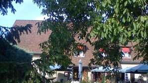 A building with a brick facade, a red roof, and a garden area with grass and trees. - Hôtel Restaurant Le relais de la Sans Fond (Fenay)