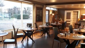 A restaurant interior with round tables and chairs, a menu board, and a view of the outside. - Hôtel Restaurant Le relais de la Sans Fond (Fenay)