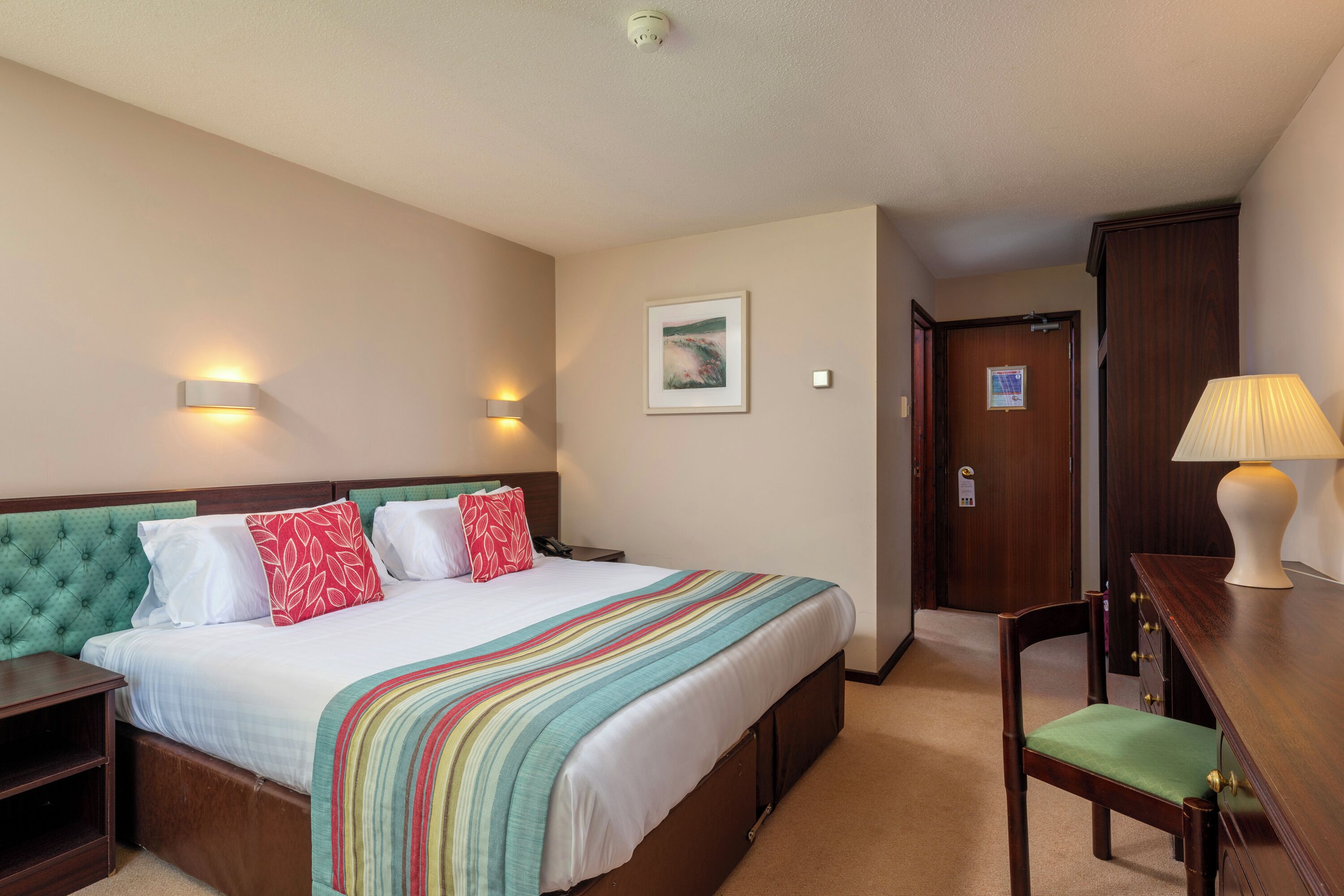 Ein Hotelzimmer mit Bett, Nachttischen, Schreibtisch, Stuhl, Lampe und einer Tür.