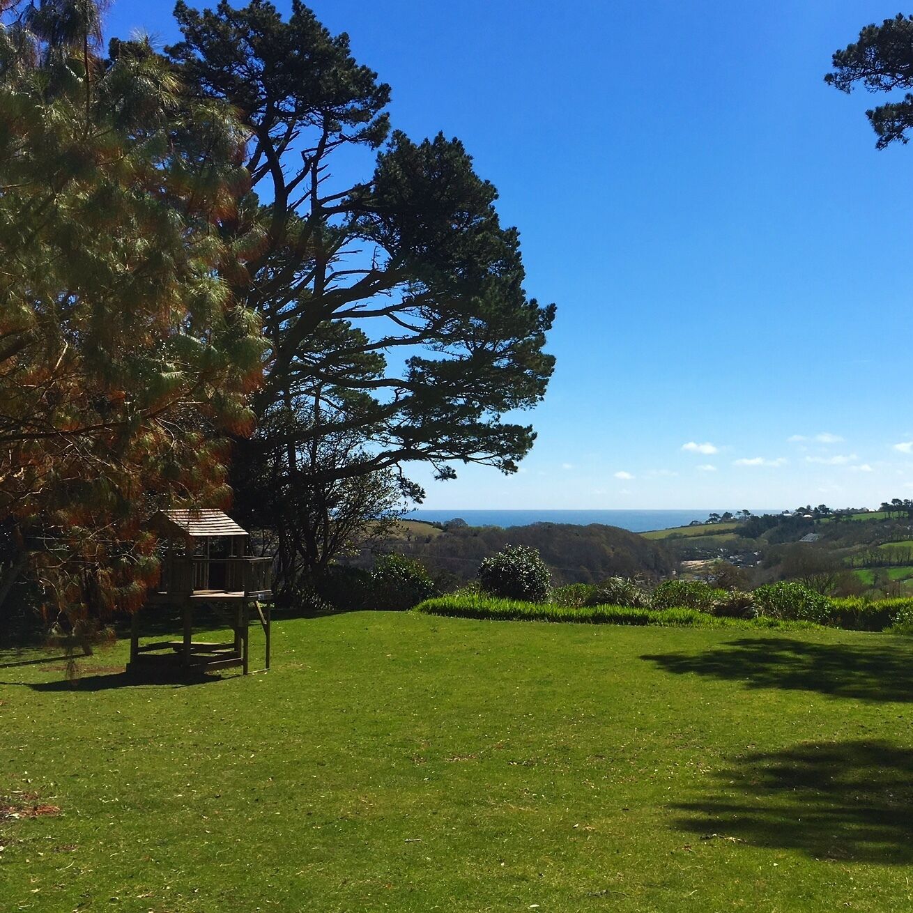 A grassy area with a wooden structure, trees, and a distant view of hills.