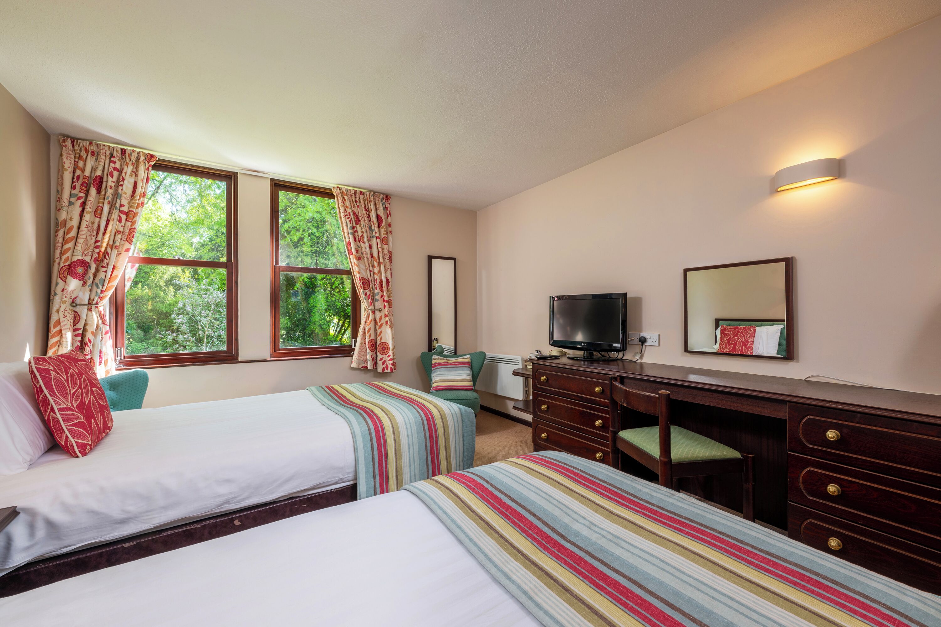 A hotel room with two beds, a TV, a desk, and a mirror.