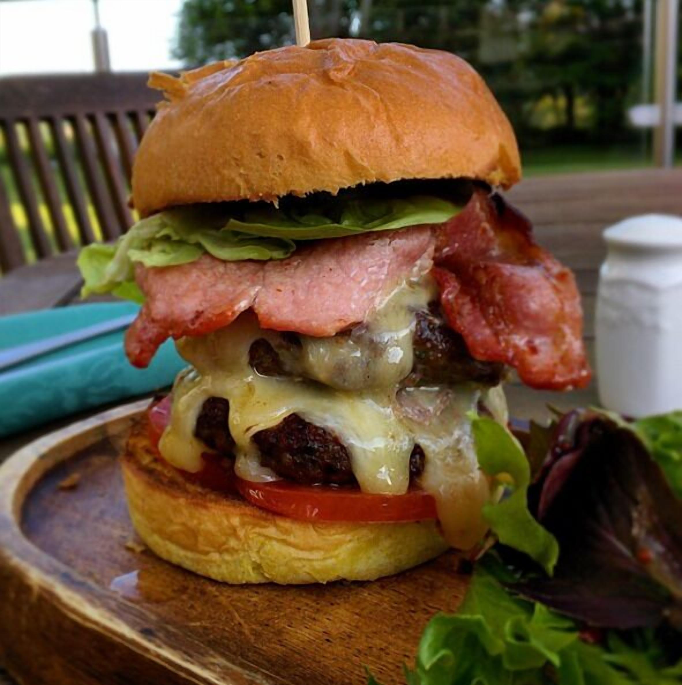 Un hamburger garni de laitue, de tomates, de fromage et de bacon, servi sur une planche en bois.