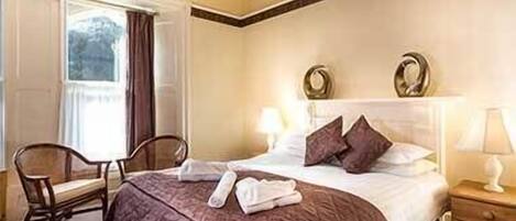 Una habitación de hotel con una cama grande, una silla, una mesita de noche y una ventana con cortinas.